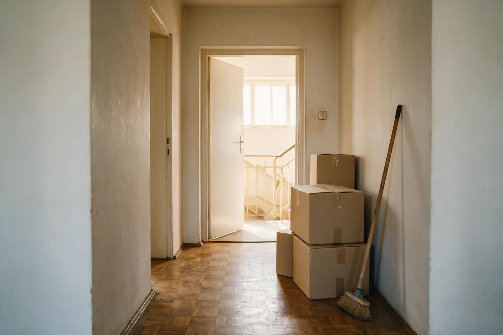 Geräumte Wohnung mit offener Tür zum Treppenhaus, gestapelte Kartons und ein Besen